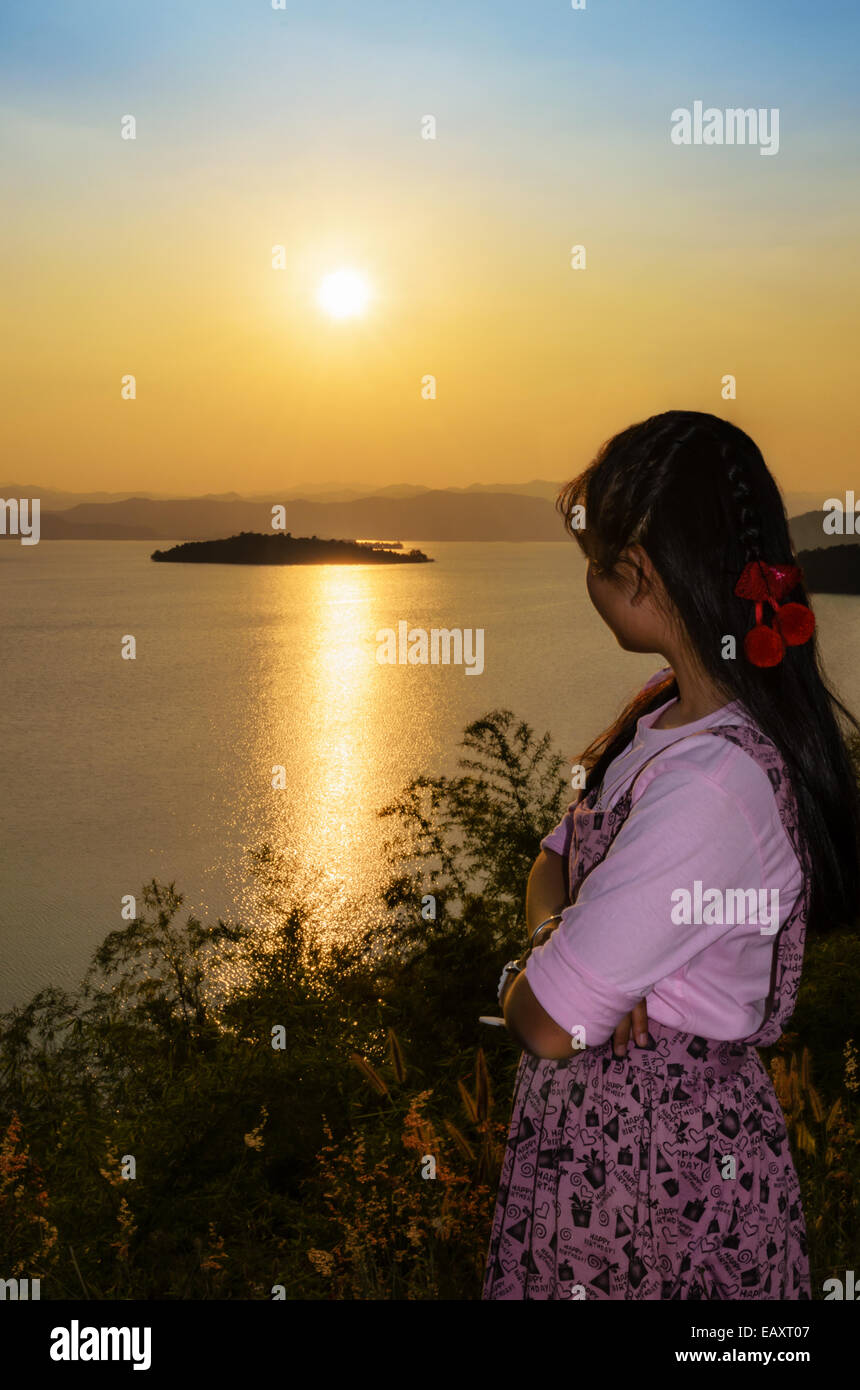 Glückliche junge Frau steht auf dem Hügel, den Sonnenuntergang über dem See im Kaeng Kra Chan National Park, Provinz Phetchaburi, Stockfoto