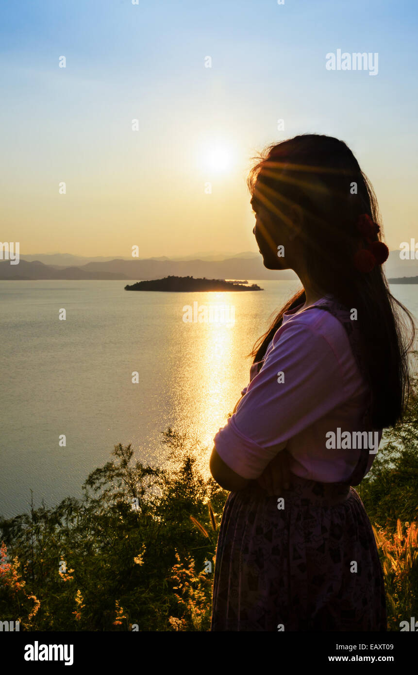 Glückliche junge Frau steht auf dem Hügel, den Sonnenuntergang über dem See im Kaeng Kra Chan National Park, Provinz Phetchaburi, Stockfoto
