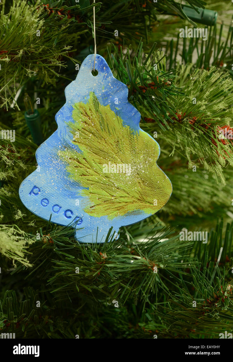 Eine handgefertigte Keramik Ornament in Form eines Weihnachtsbaumes mit einem grünen Ast, blauen Himmel und das Wort Frieden gemalt Stockfoto