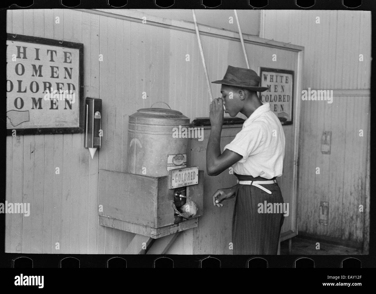 Dieses Foto aus den 1930er Jahren zeigt einen afroamerikanischen Mann, der aus einem ausgewiesenen „farbigen“ Wasserkühler an einem Straßenbahnterminal in Oklahoma trinkt, was die Rassentrennung dieser Zeit widerspiegelt. Stockfoto