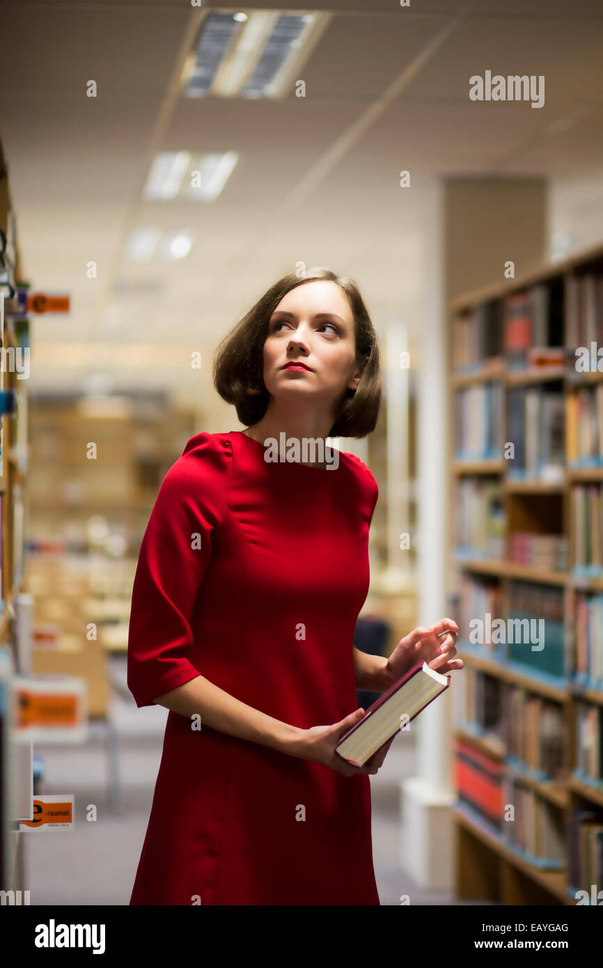 Junge Frau in Bibliothek zwischen den Regalen mit Buch Stockfoto