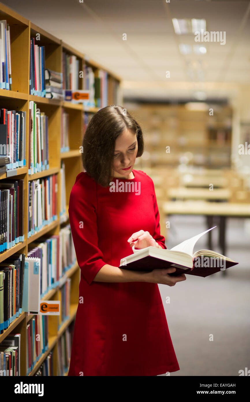 Junge Frau in der Bibliothek in der Nähe von Regalen mit Buch Stockfoto