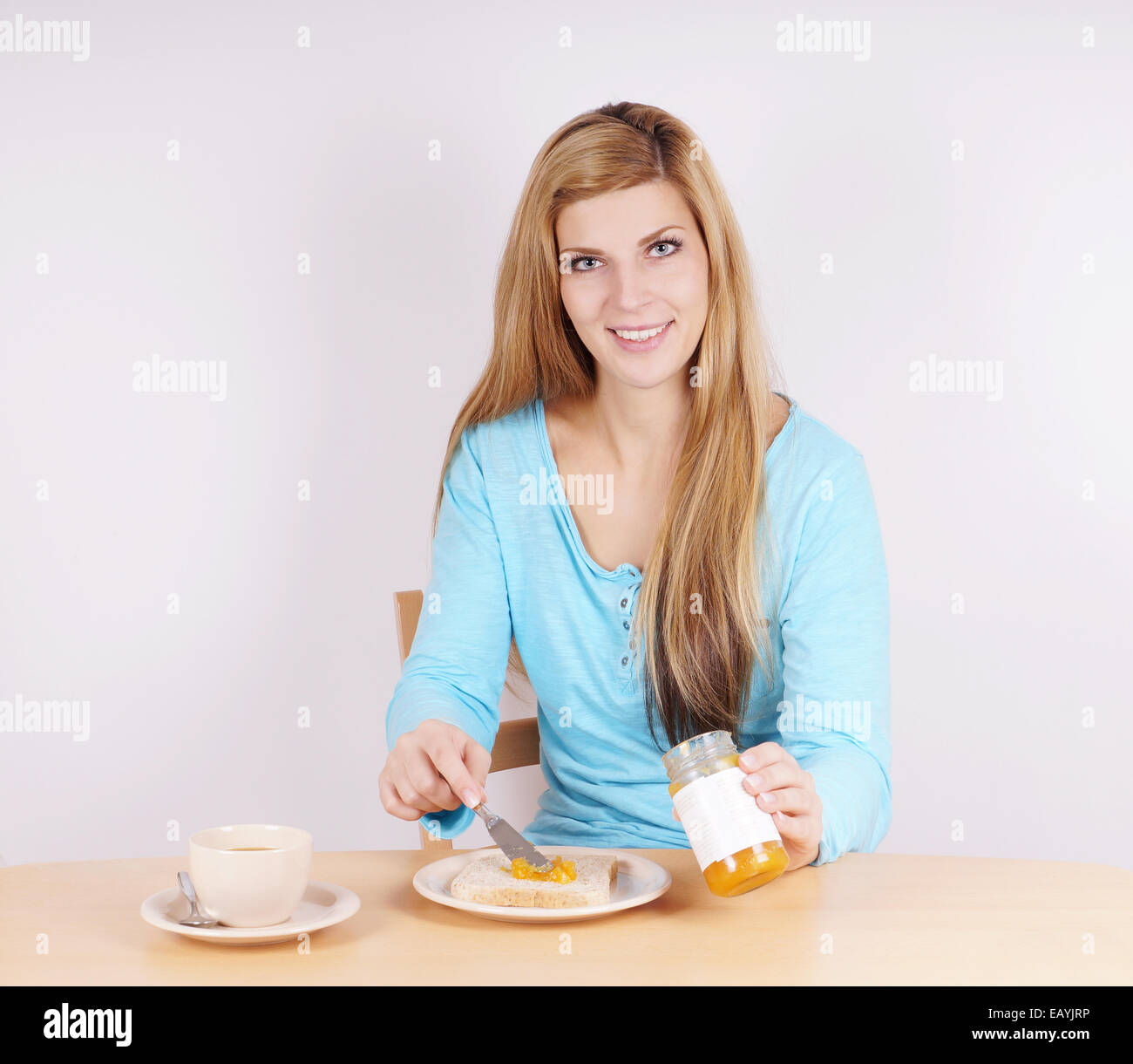 junge Frau, die Verbreitung von Marmelade auf ihrem Toast am Frühstückstisch Stockfoto