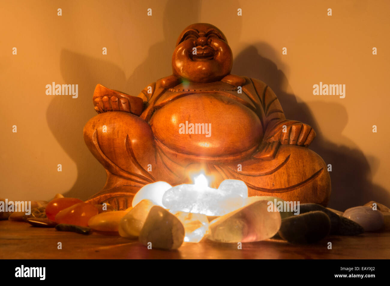 Eine hölzerne Statue des lachenden Buddha wird durch eine Kerzenlicht reflektiert in einigen Edelsteinen beleuchtet. Stockfoto