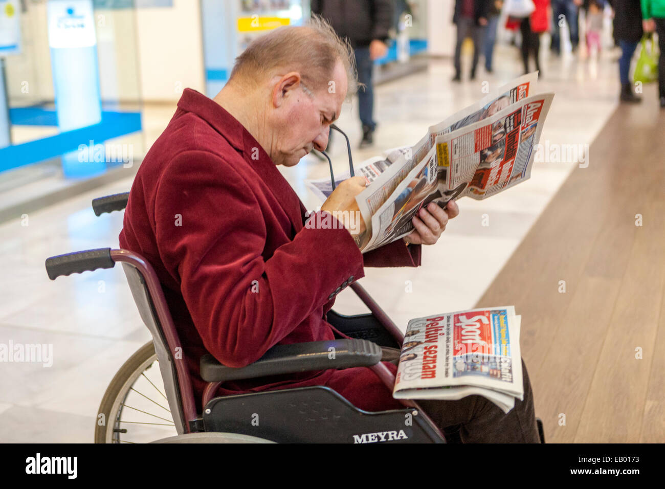 Ein älterer Mann im Rollstuhl liest eine Zeitung in einem Einkaufszentrum älterer Erwachsener im Einkaufszentrum Stockfoto