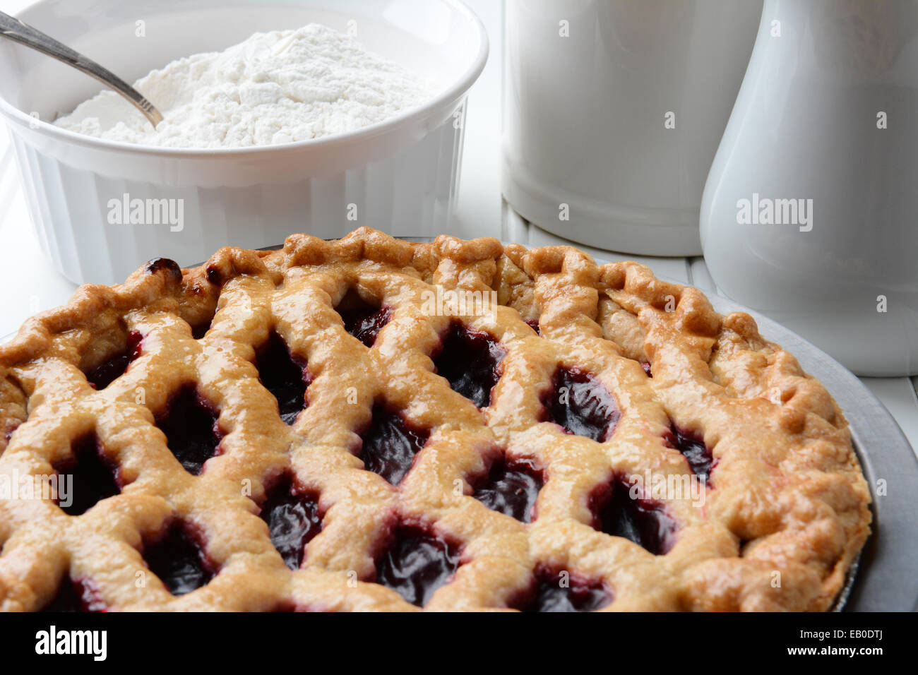 Hohen Winkel Schuss einen frisch gebackenen Kirschkuchen mit einem Gitter-Kruste. Eine Schüssel mit Mehl und Krüge füllen Sie den Hintergrund. Horizontale f Stockfoto