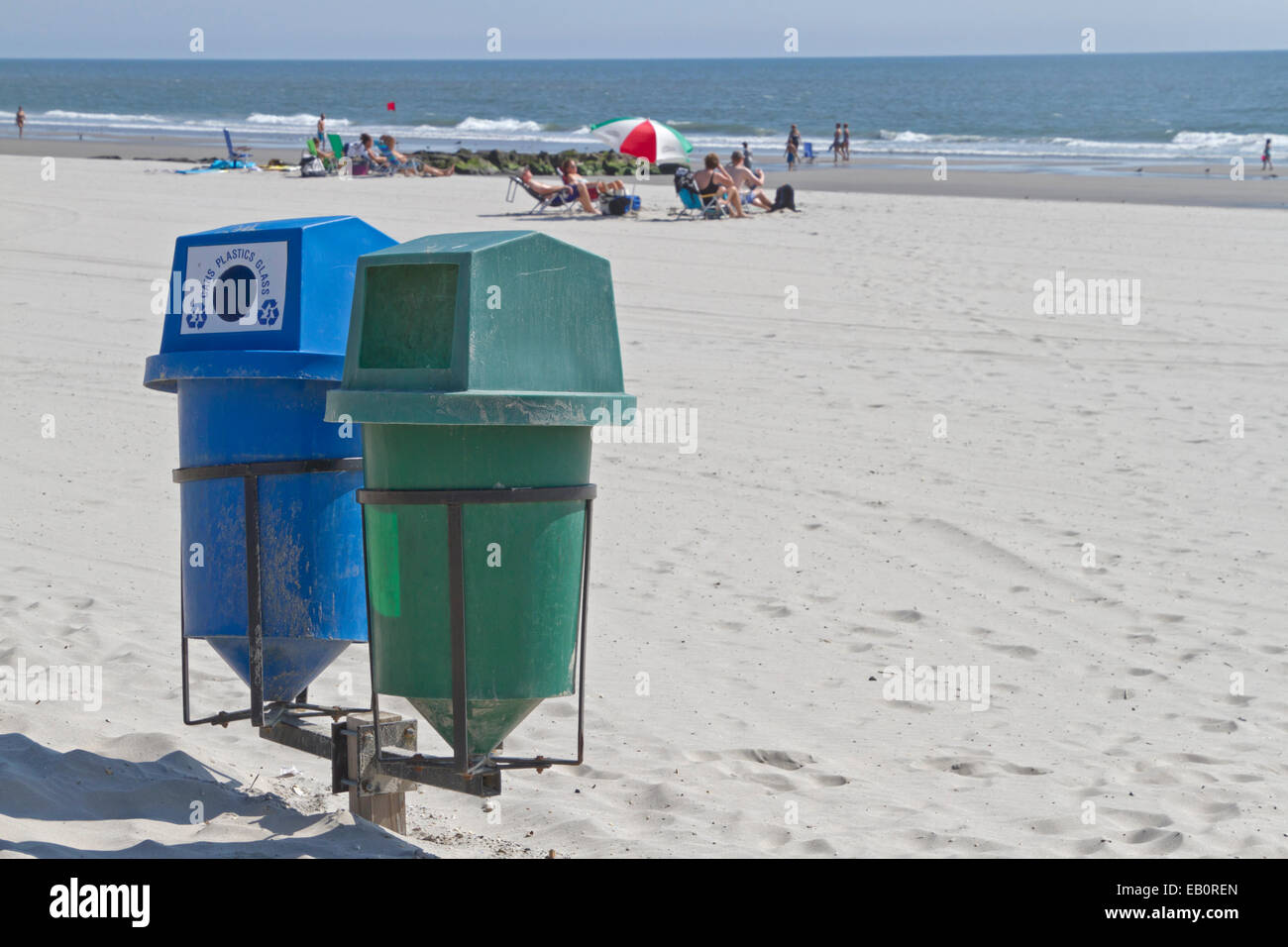 Zwei Kästen im Vordergrund auf einem sauberen Strand mit Sonnenbaden am Meer in der Ferne zu recyceln Stockfoto