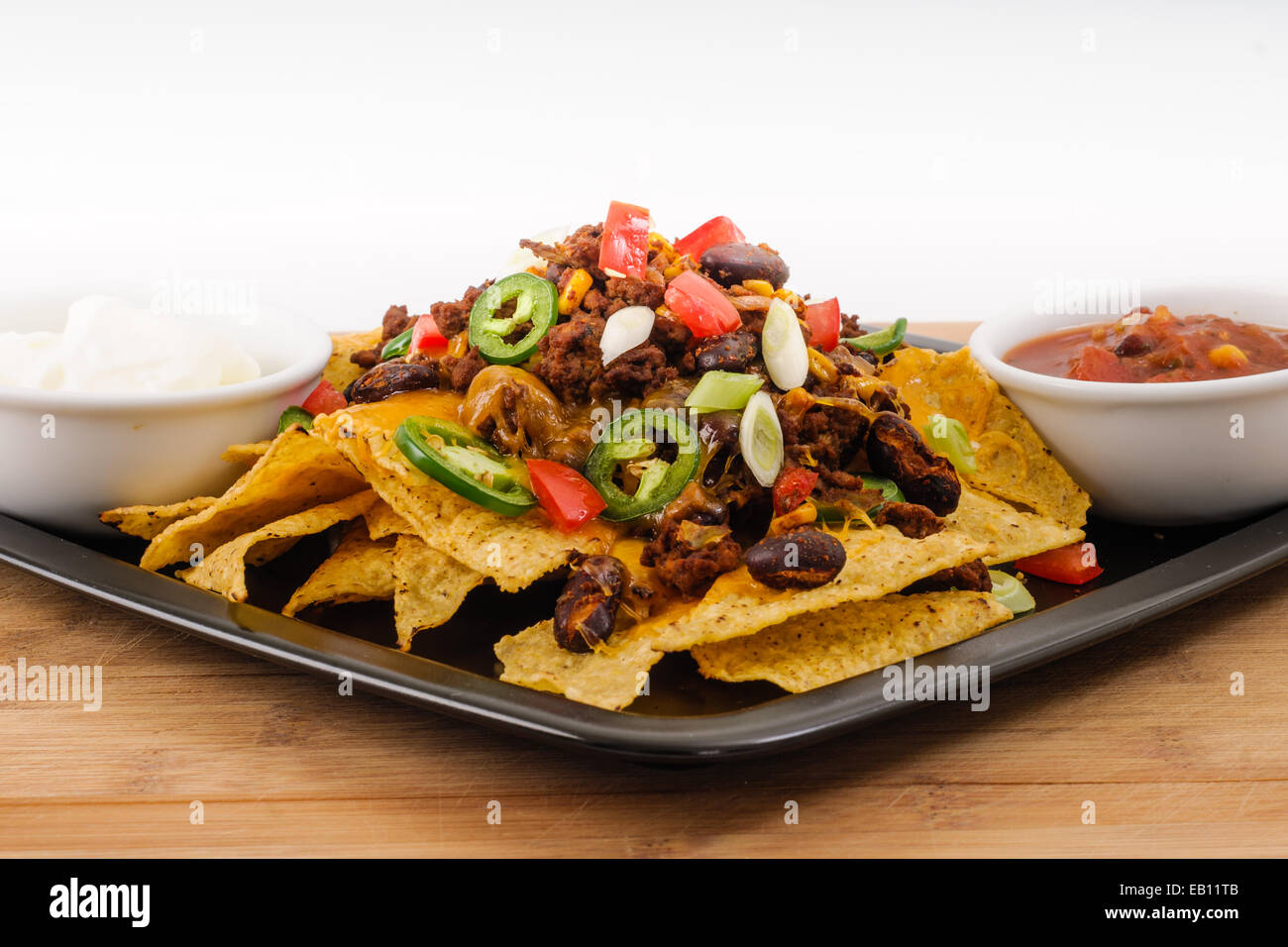 Chili und Cheddar Käse Nacho Teller mit frischen Tomaten, Zwiebeln, Jalapeño Paprika, Sauerrahm und Salsa Stockfoto