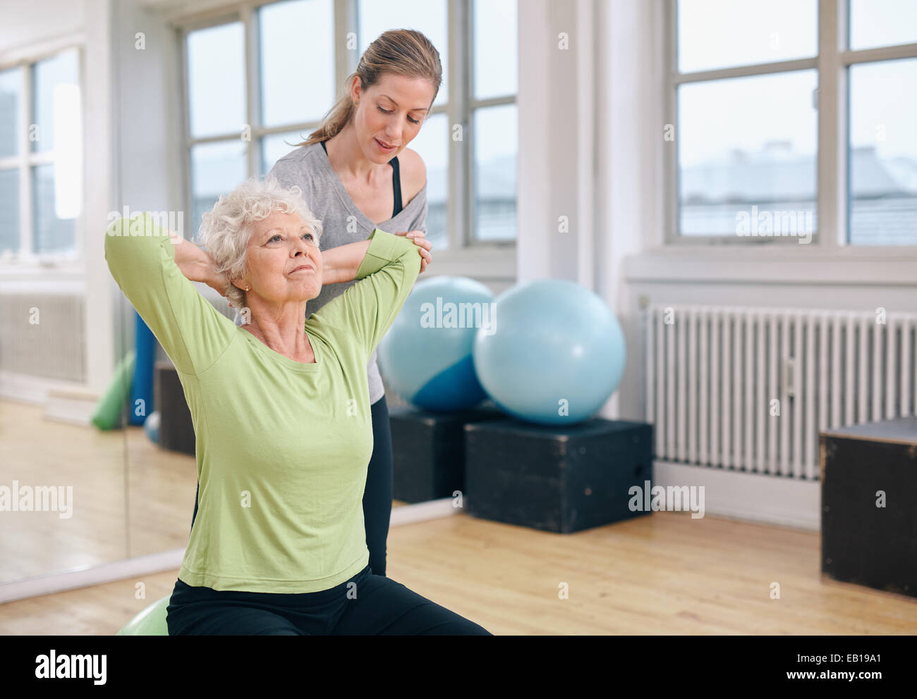 Frauen in Führungspositionen, leichtes Pilates-Training für die Rückenmuskulatur mit Trainer Unterstützung zu tun. Trainer helfen senior Frau im Fitness-Studio trainieren. Stockfoto
