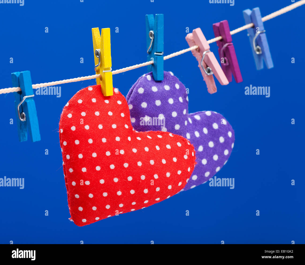 zwei Herzen hängen an einer Wäscheleine mit Wäscheklammern, konzentrieren sich auf rot. Blauer Hintergrund Stockfoto