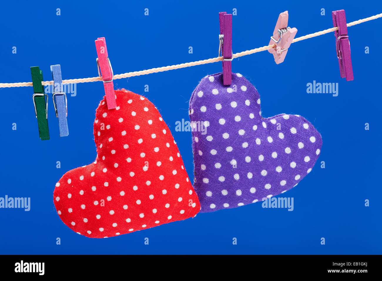 zwei Herzen hängen an einer Wäscheleine mit Wäscheklammern, blauer Hintergrund Stockfoto