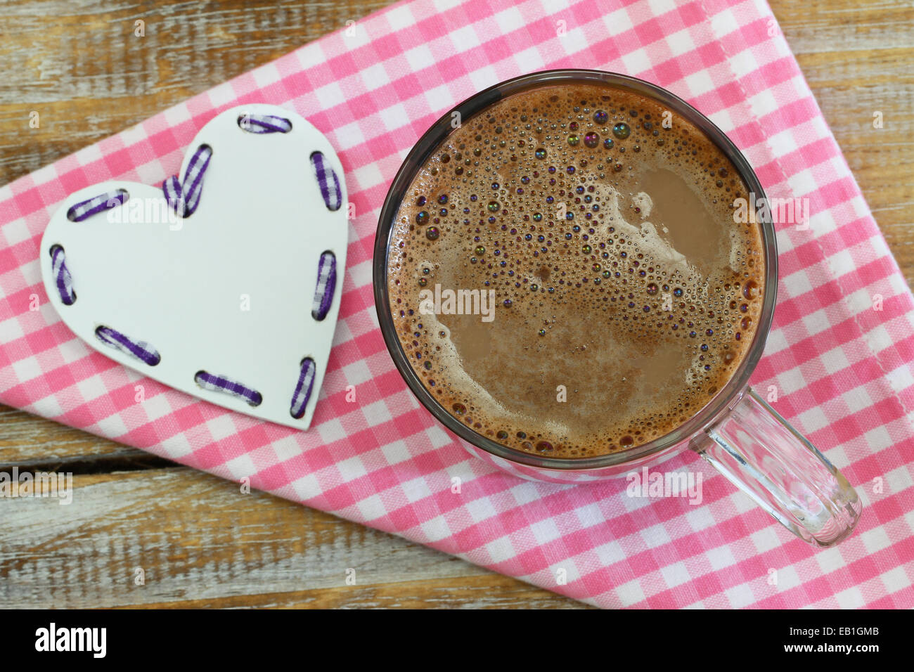 Heiße Schokolade im Glas auf rosa karierten Stoff und weißes Herz Stockfoto