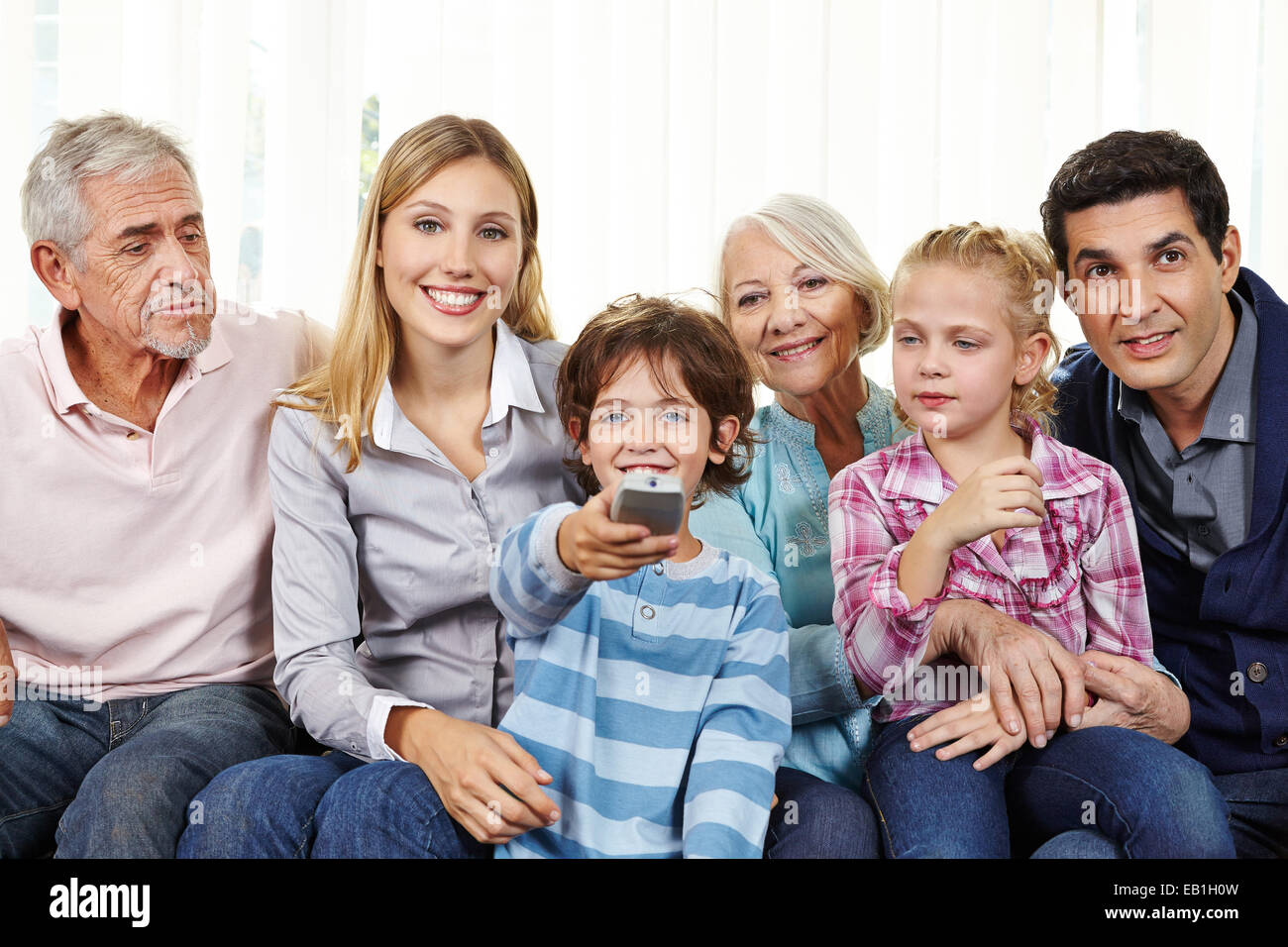 Große, glückliche Familie vor dem Smart Fernseher mit Fernbedienung im Wohnzimmer Stockfoto