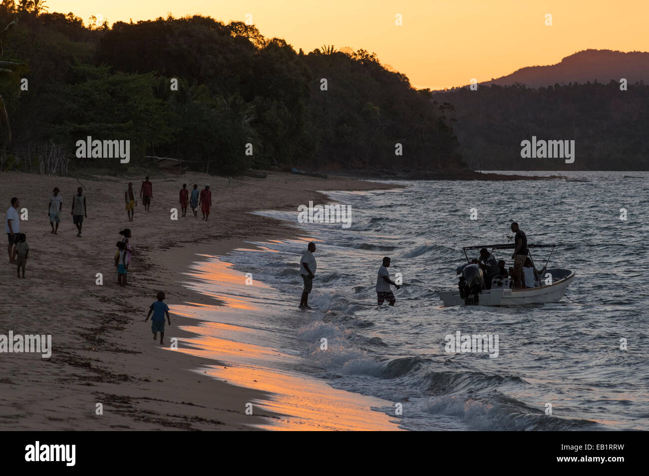 Madagassische Einheimischen zu Fuß am Strand bei Sonnenuntergang mit Boot Stockfoto
