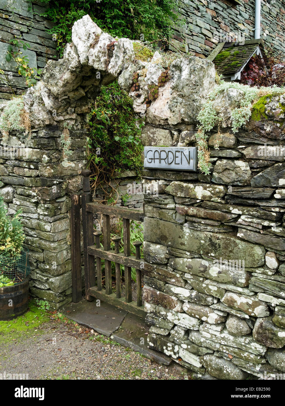 Alte Schieferwand aus trockenem Stein mit Bogengang über Holztor in den Garten Stockfoto