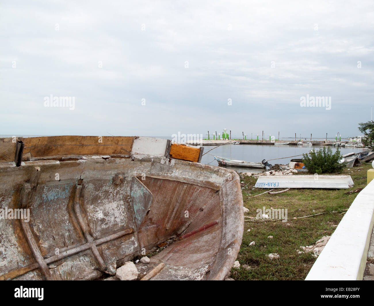 Altes Boot an der Seite an Land gedreht mit dem Melecon im Vordergrund und kleinere Boote in einem Hafen im Hintergrund, Campeche, Mexiko. Stockfoto