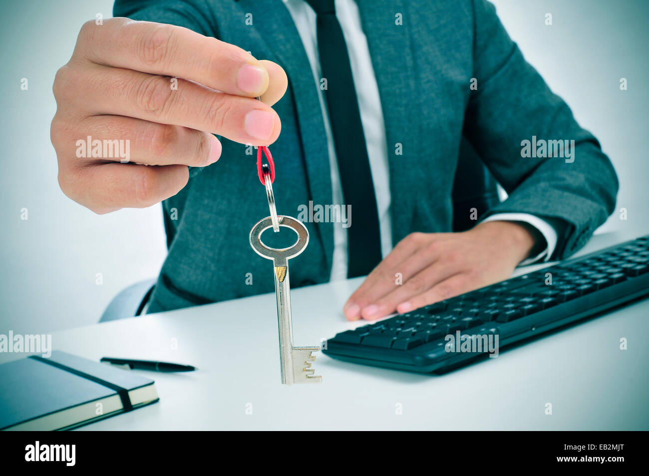 ein Mann in Anzug sitzt in einem Schreibtisch geben den Schlüssel für dem Betrachter Stockfoto