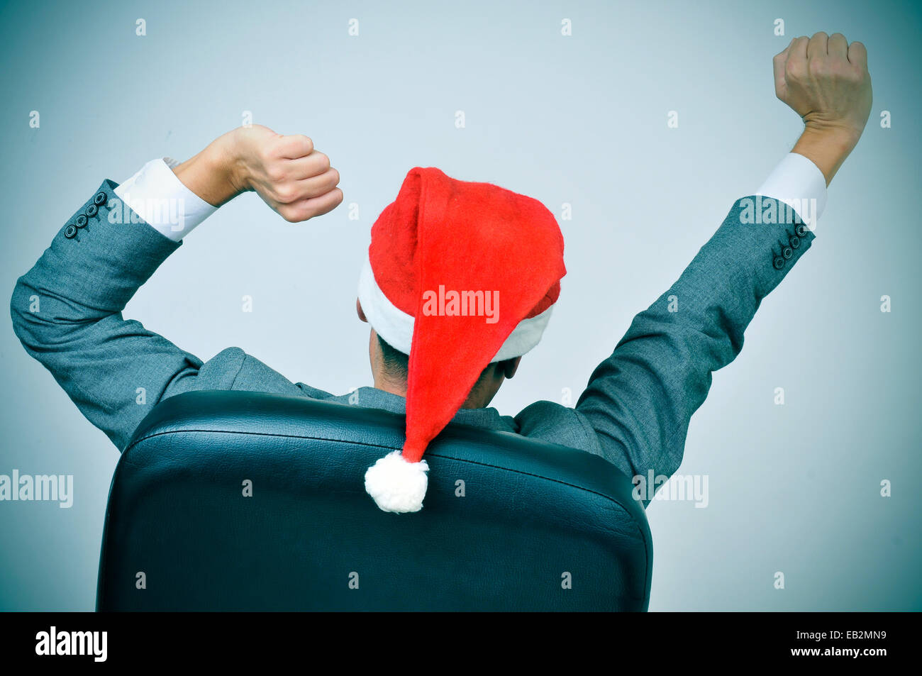 ein Mann in Anzug mit einer Nikolausmütze, streckte die Arme in seinem Bürostuhl Stockfoto