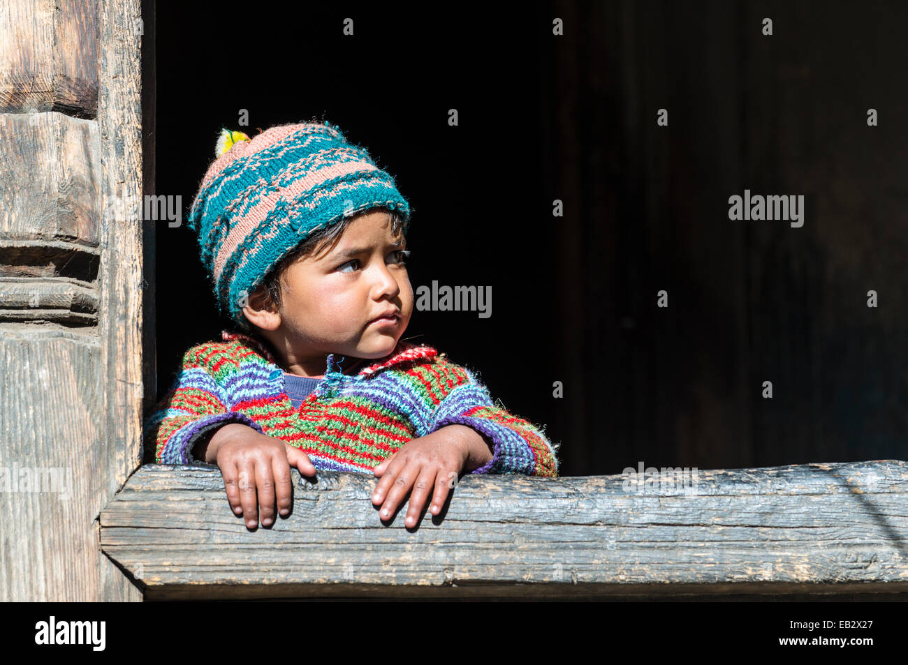 Ein kleines Kind, der Blick aus dem Fenster eines Holzhauses, Chitkul, Himachal Pradesh, Indien Stockfoto