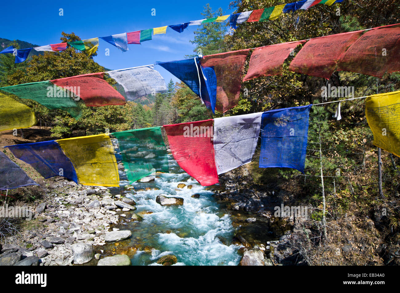 Bunte Gebetsfahnen überfliegen Türkis Stromschnellen in einem alpinen Fluss. Stockfoto