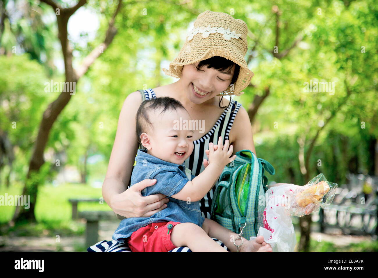 Lächelnde Mutter, die im Park sitzt und ihren Sohn Brot isst Stockfoto