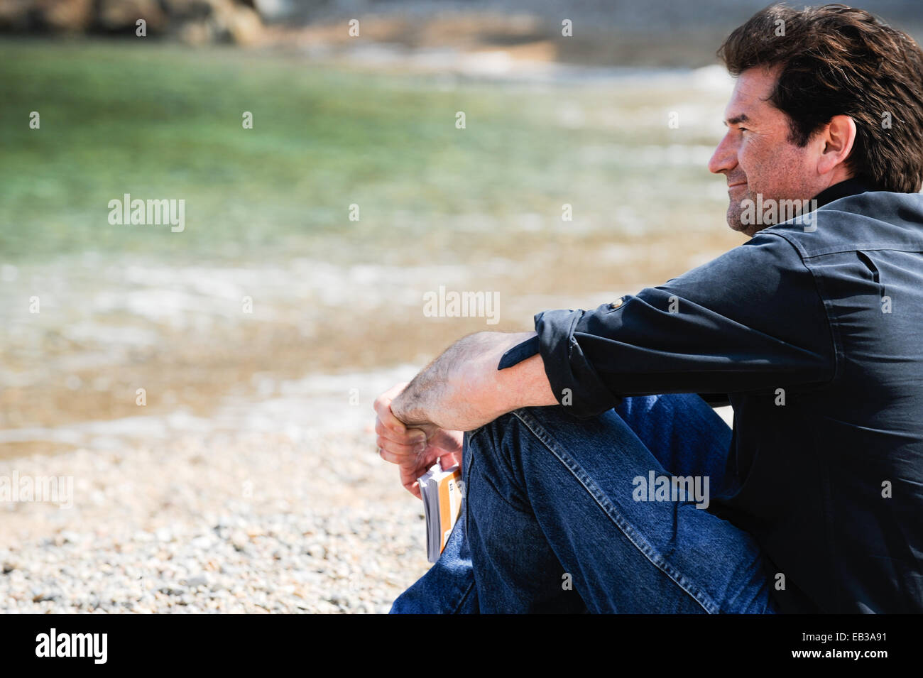 Mann sitzt am Strand mit einem Reiseführer, Sa Tuna Strand, Begur, Girona, Katalonien, Spanien Stockfoto