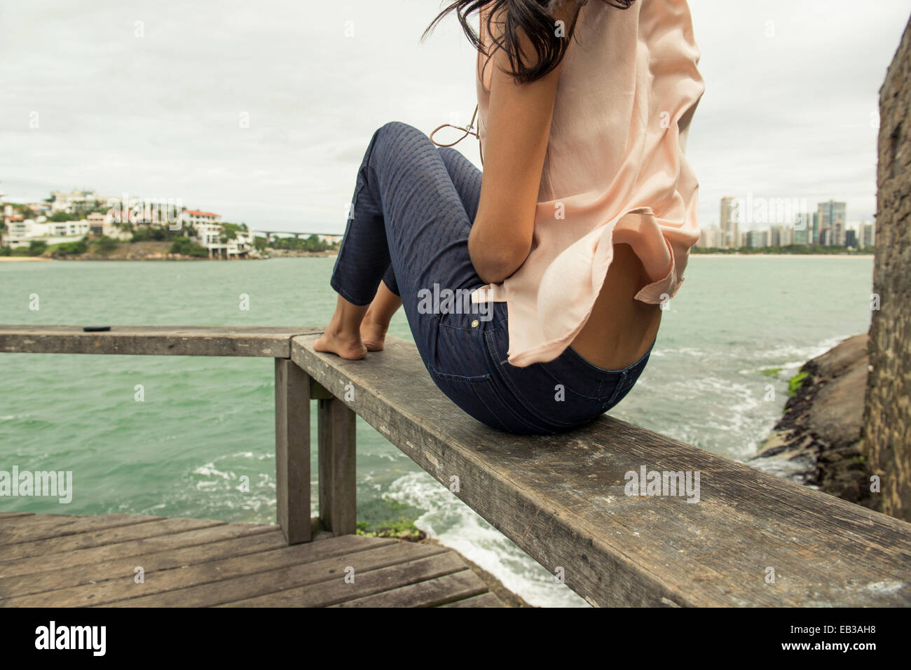 Frau sitzt auf dem Geländer mit Blick auf städtischen Hafen Stockfoto