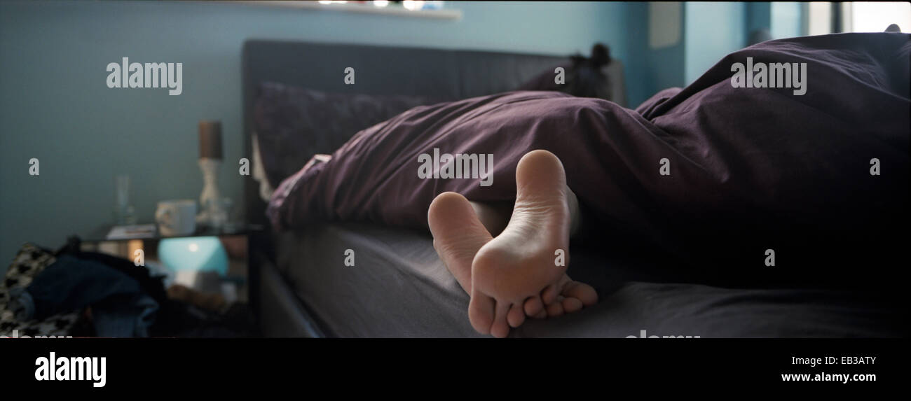 Nahaufnahme der Füße einer Person im Bett, die unter einer Bettdecke herausragen Stockfoto