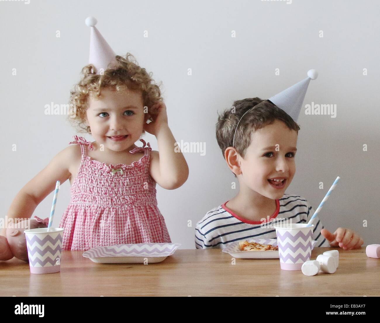 Porträt von zwei Kindern, die an einem Tisch sitzen, essen und trinken auf einer Geburtstagsfeier Stockfoto