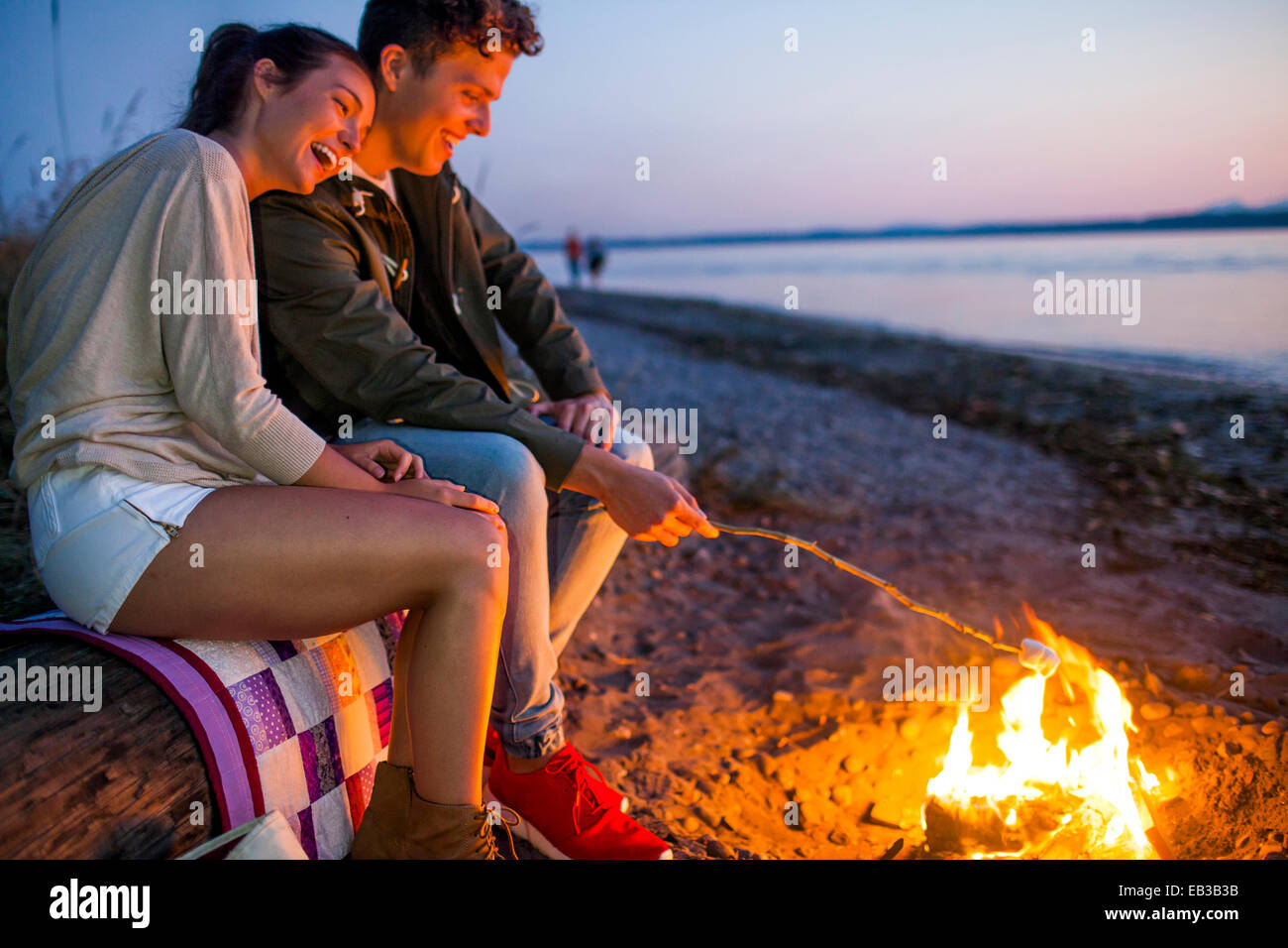 Kaukasische paar Rösten Marshmallows am Feuer am Strand Stockfoto