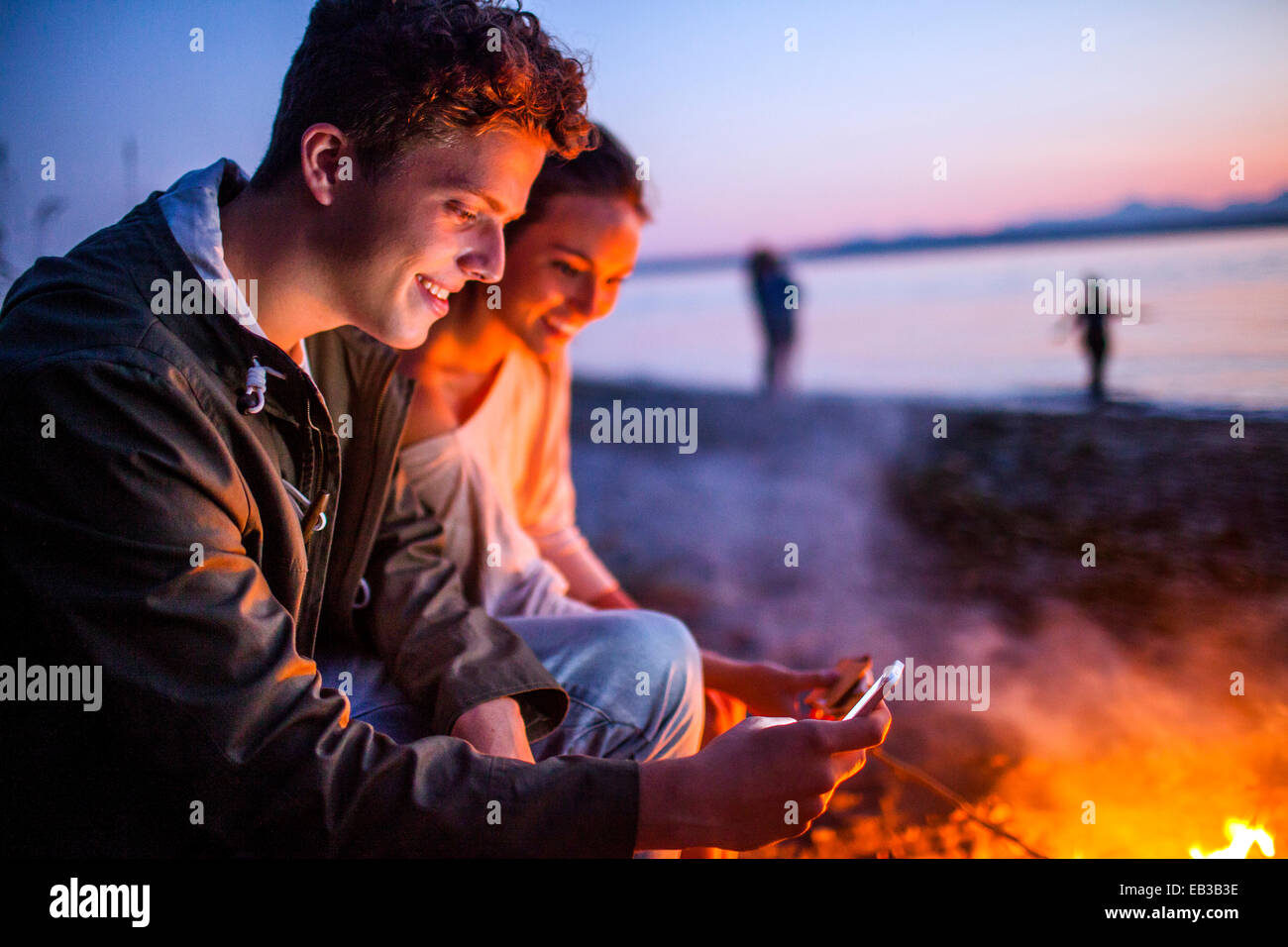 Kaukasische paar mit Handy zusammen in der Nähe von Feuer am Strand Stockfoto