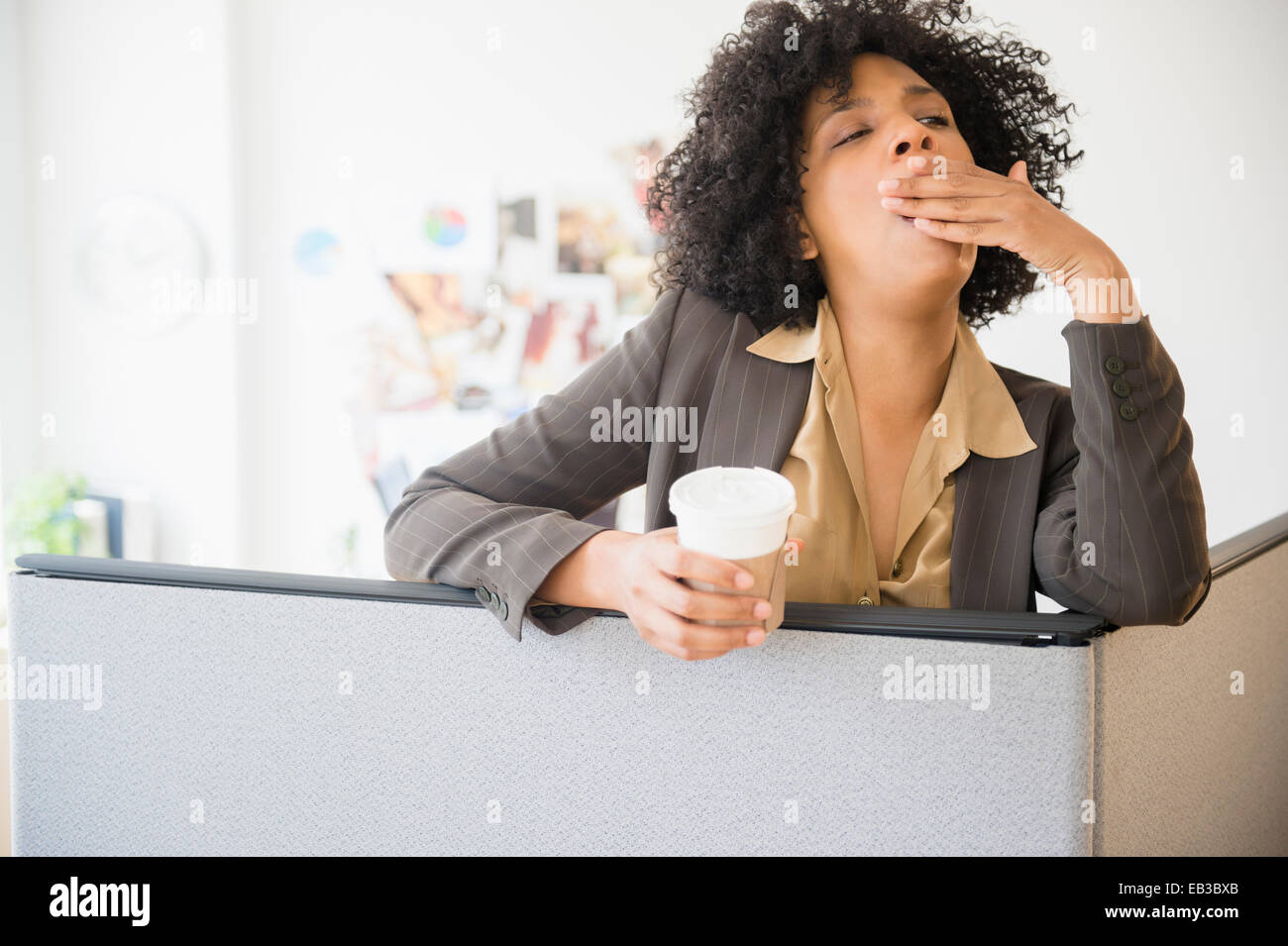 Geschäftsfrau mit Tasse Kaffee Gähnen in Kabine Stockfoto