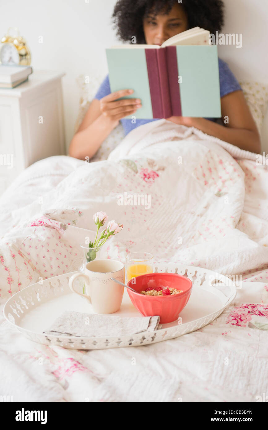 Frau-Lesebuch und mit Frühstück im Bett Stockfoto