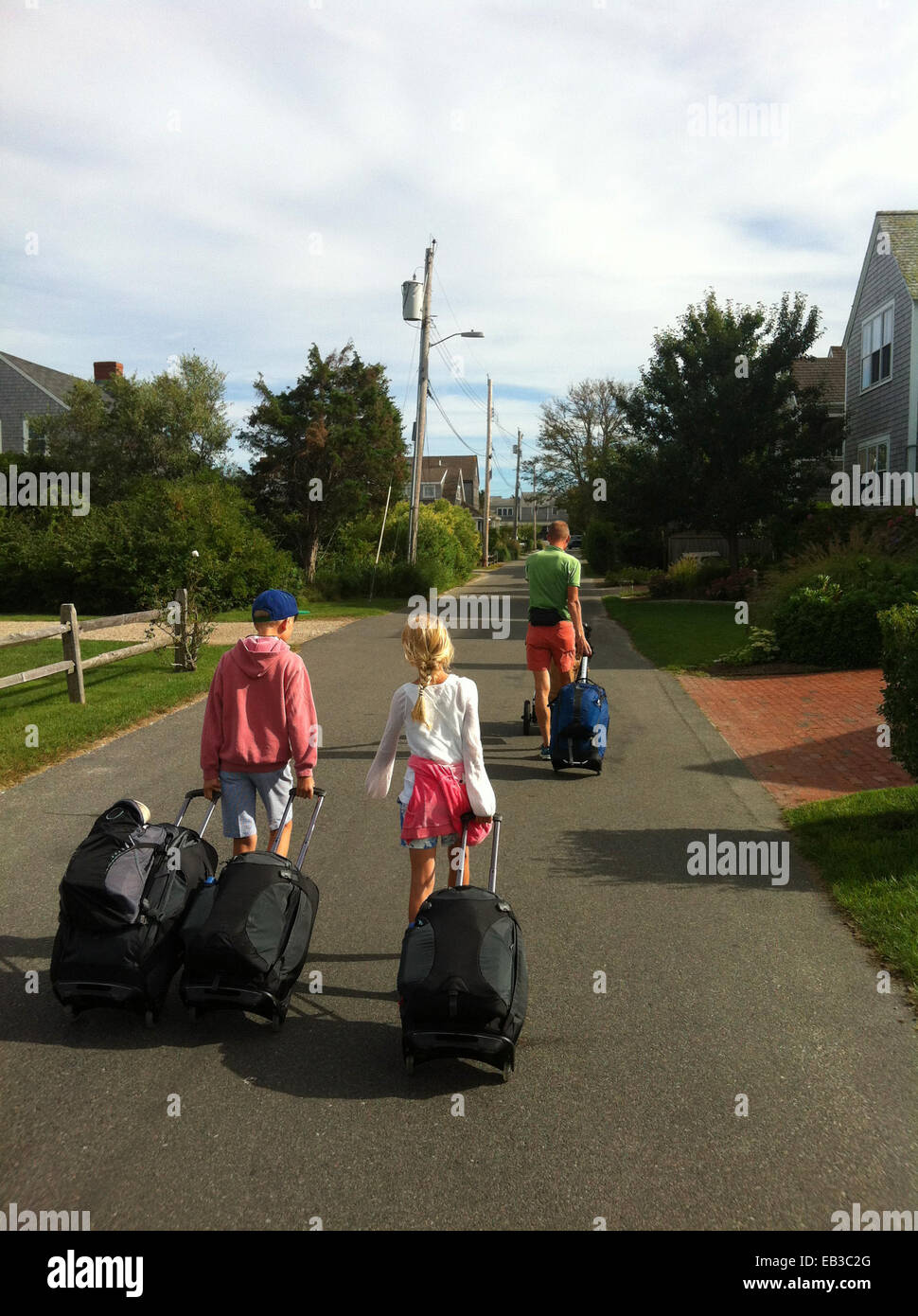 Vater mit zwei Kindern, die die Straße hinunter laufen und Koffer ziehen, Norwegen Stockfoto