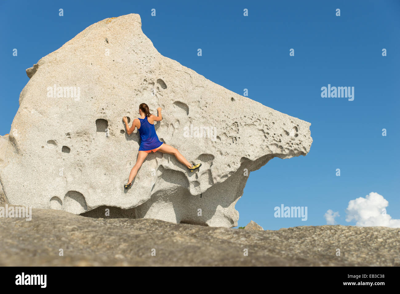 Rückansicht einer Frau, die einen großen Felsen klettert, Korsika, Frankreich Stockfoto