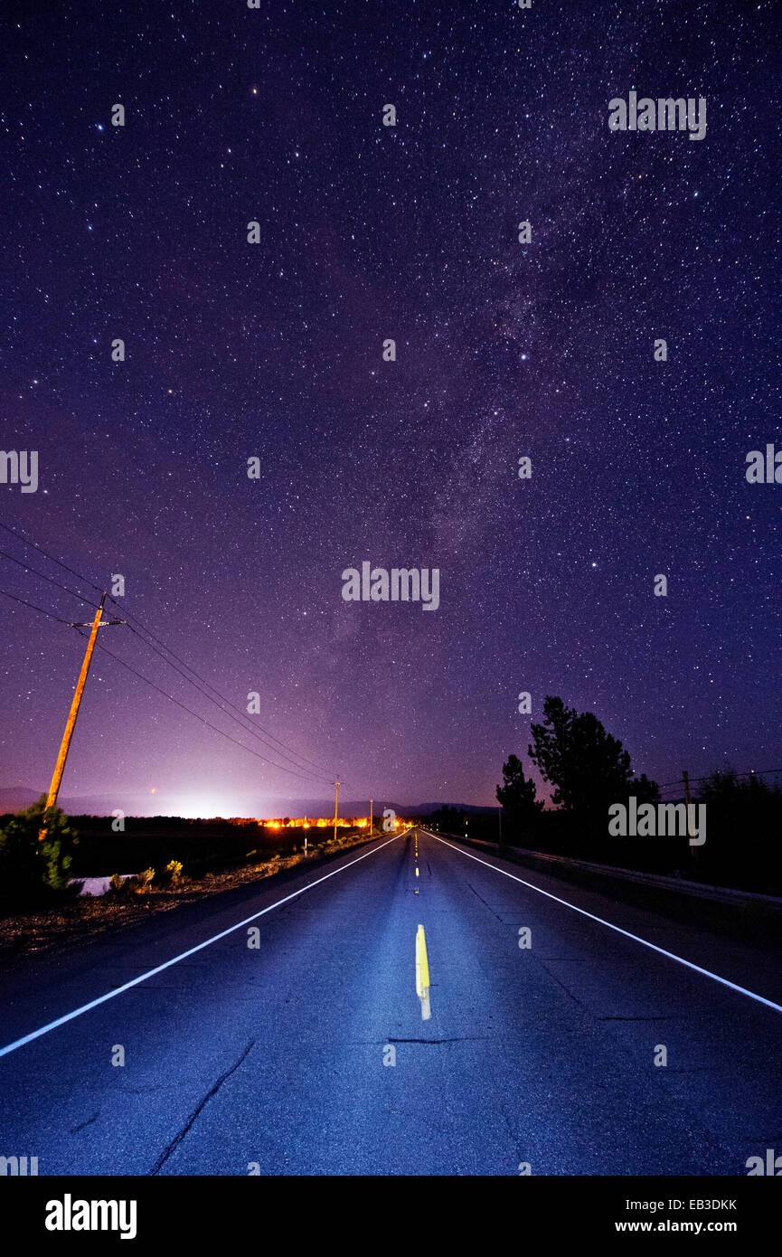 Asphaltierte Straße unter Sternenhimmel von Scheinwerfern beleuchtet Stockfoto