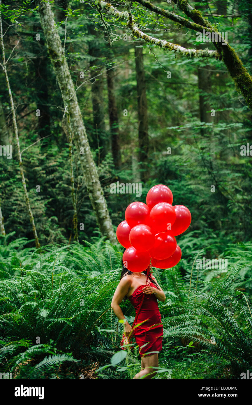 Koreanische Frau mit roten Luftballons in üppigen Wald Stockfoto