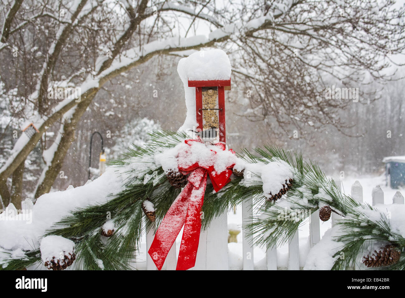 Wintergarten Vogelfutterhäuschen und rote Weihnachtsdekorationen Gartenvogelfutterhäuschen, weißer Zaun mit Girlande und Schnee, Monroe Twp., New Jersey, USA Stockfoto
