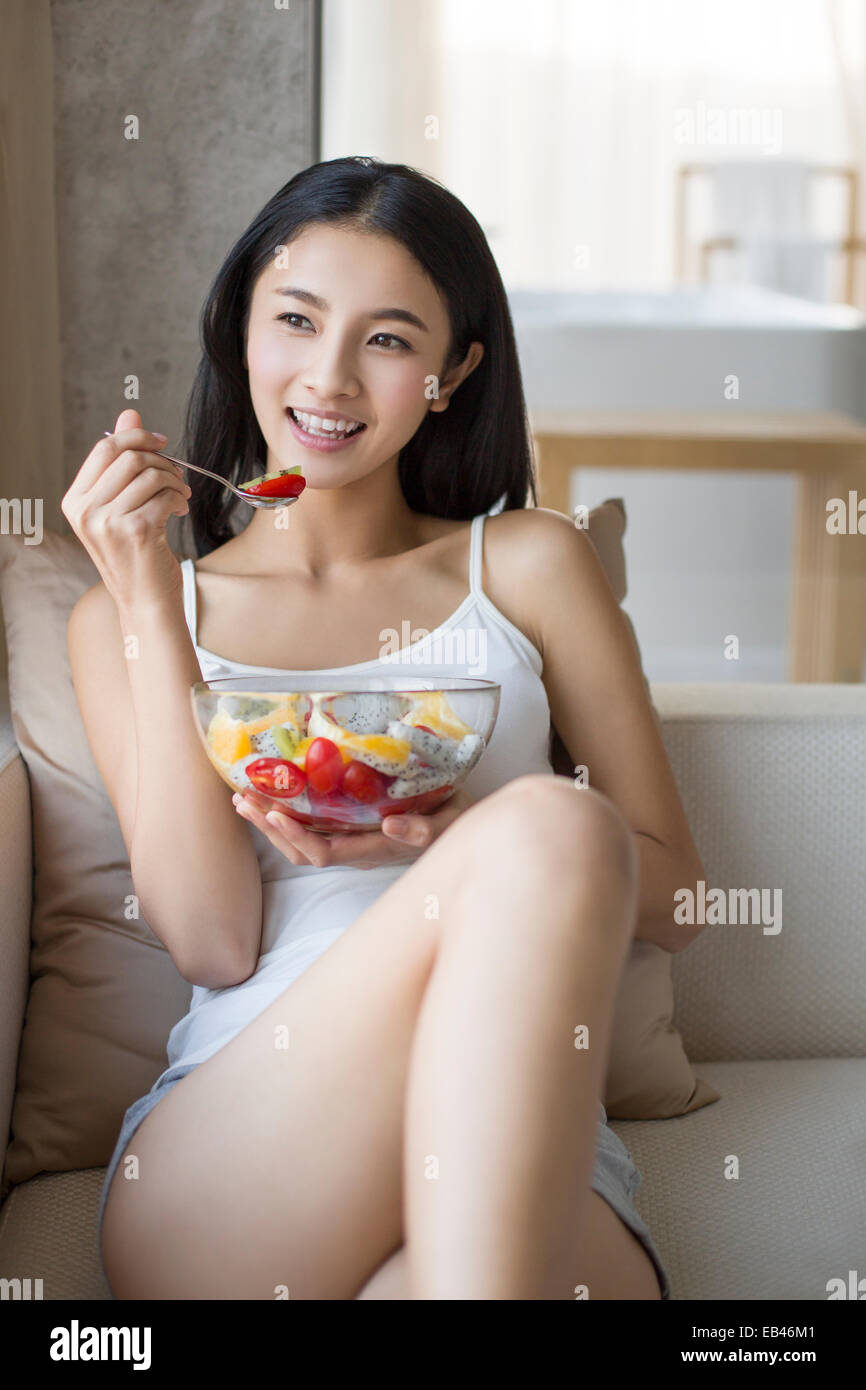 Junge Frau Essen Obstsalat auf sofa Stockfoto