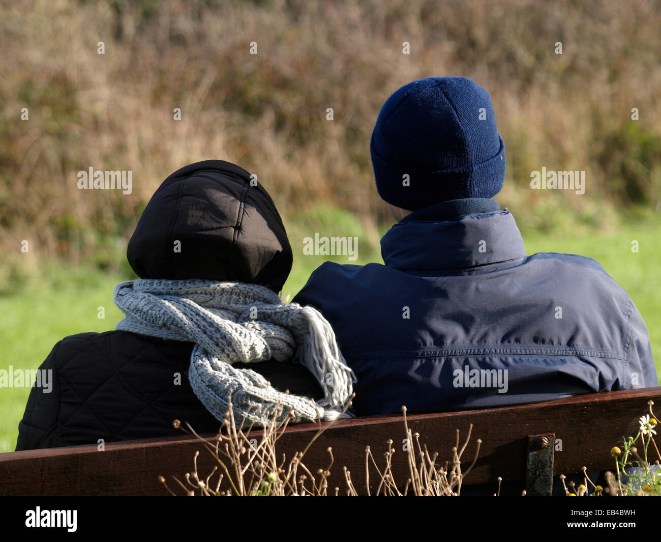 Erwachsenes paar saß auf einer öffentlichen Bank im Winter, Padstow, Cornwall, UK Stockfoto