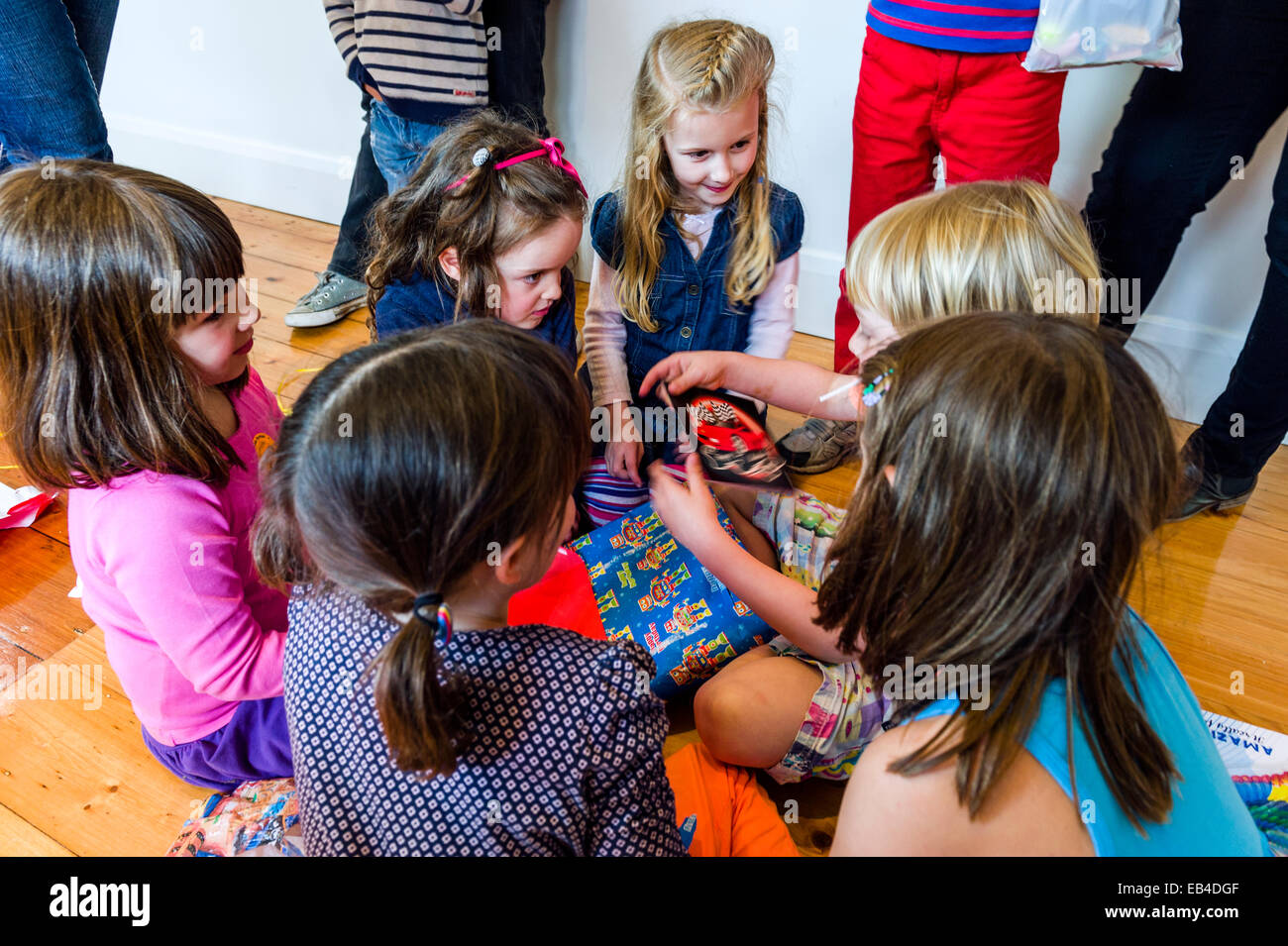 Ein Junge öffnet seine Geburtstagsgeschenke, umgeben von einer Gruppe von Freundinnen. Stockfoto