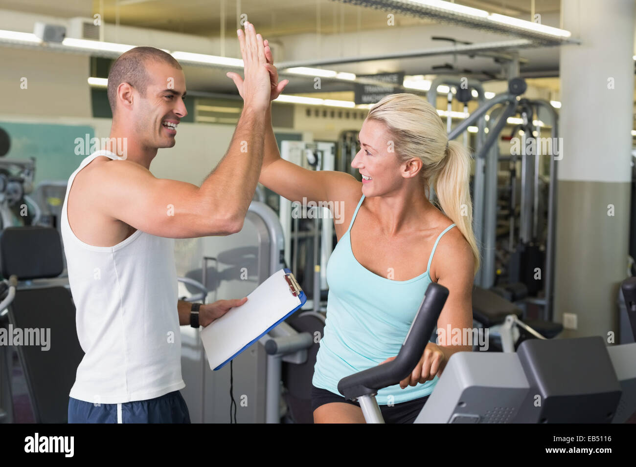 Trainer geben hohe fünf, seinen Mandanten auf Heimtrainer in Turnhalle Stockfoto