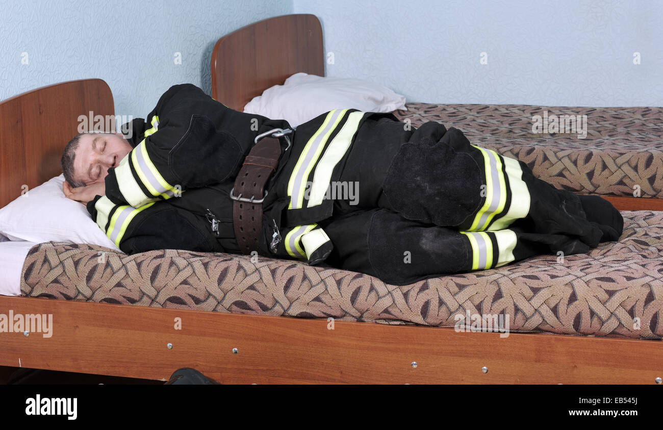 Gekleidete schlafenden Feuerwehrmann liegen auf dem Bett im Zimmer Stockfoto