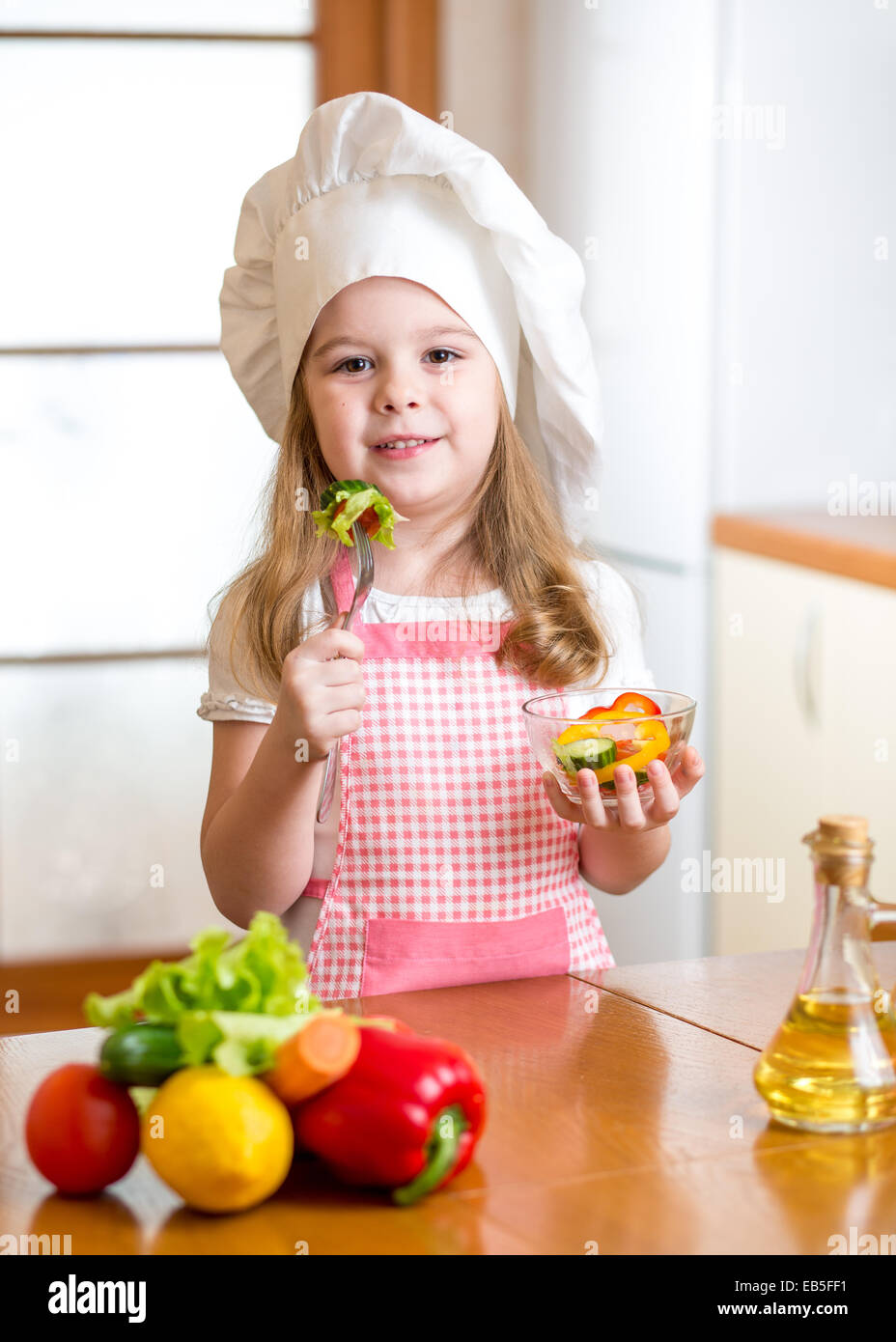 Kind Mädchen in Koch Hut Essen Gemüse Stockfoto