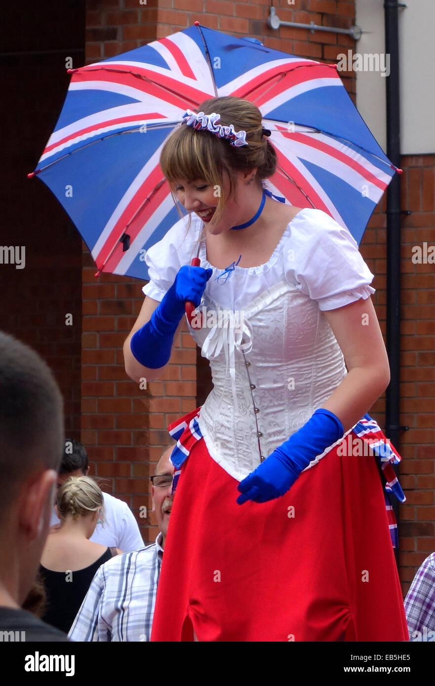 Frau im Kostüm auf Stelzen halten ein Union Jack-Regenschirm, Stourbridge Carnvial, West Midlands, England, UK Stockfoto