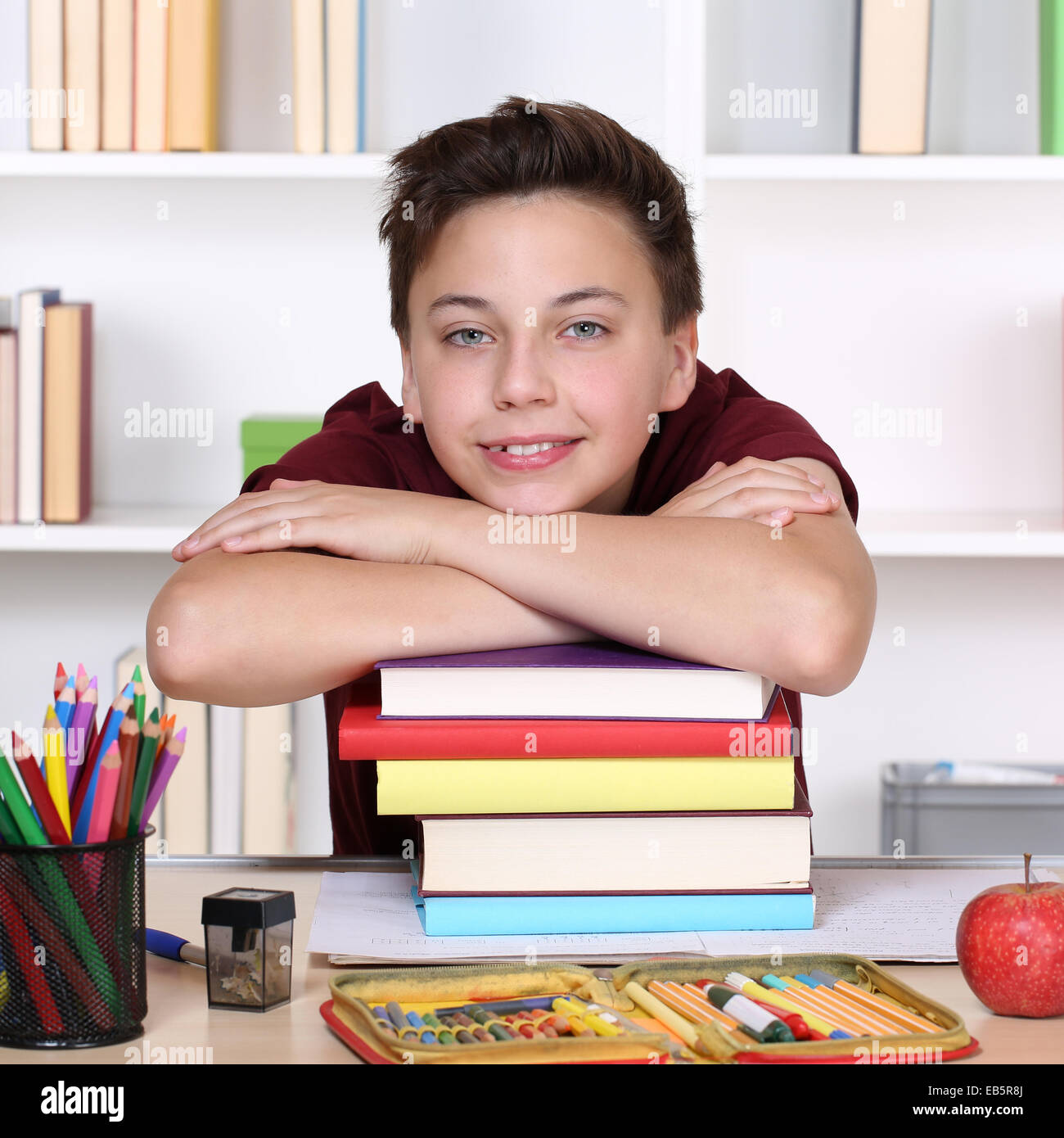 Lächelnde junge Studentin auf einem Stapel Bücher, die Hausaufgaben in der Schule Stockfoto