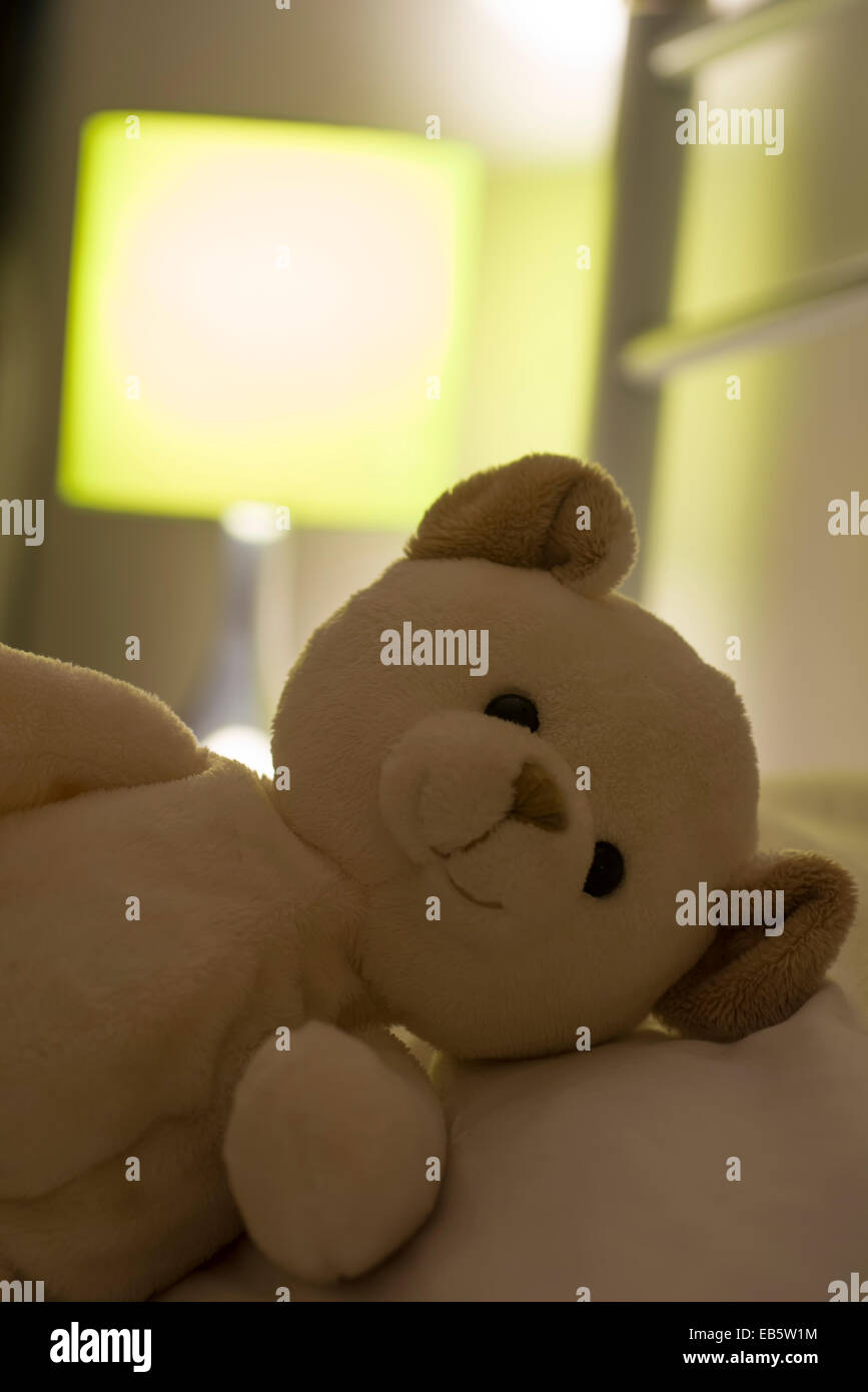 Des Kindes Teddybär Verlegung auf einem weißen Bett mit einer beleuchteten grüne Lampe im Hintergrund Stockfoto