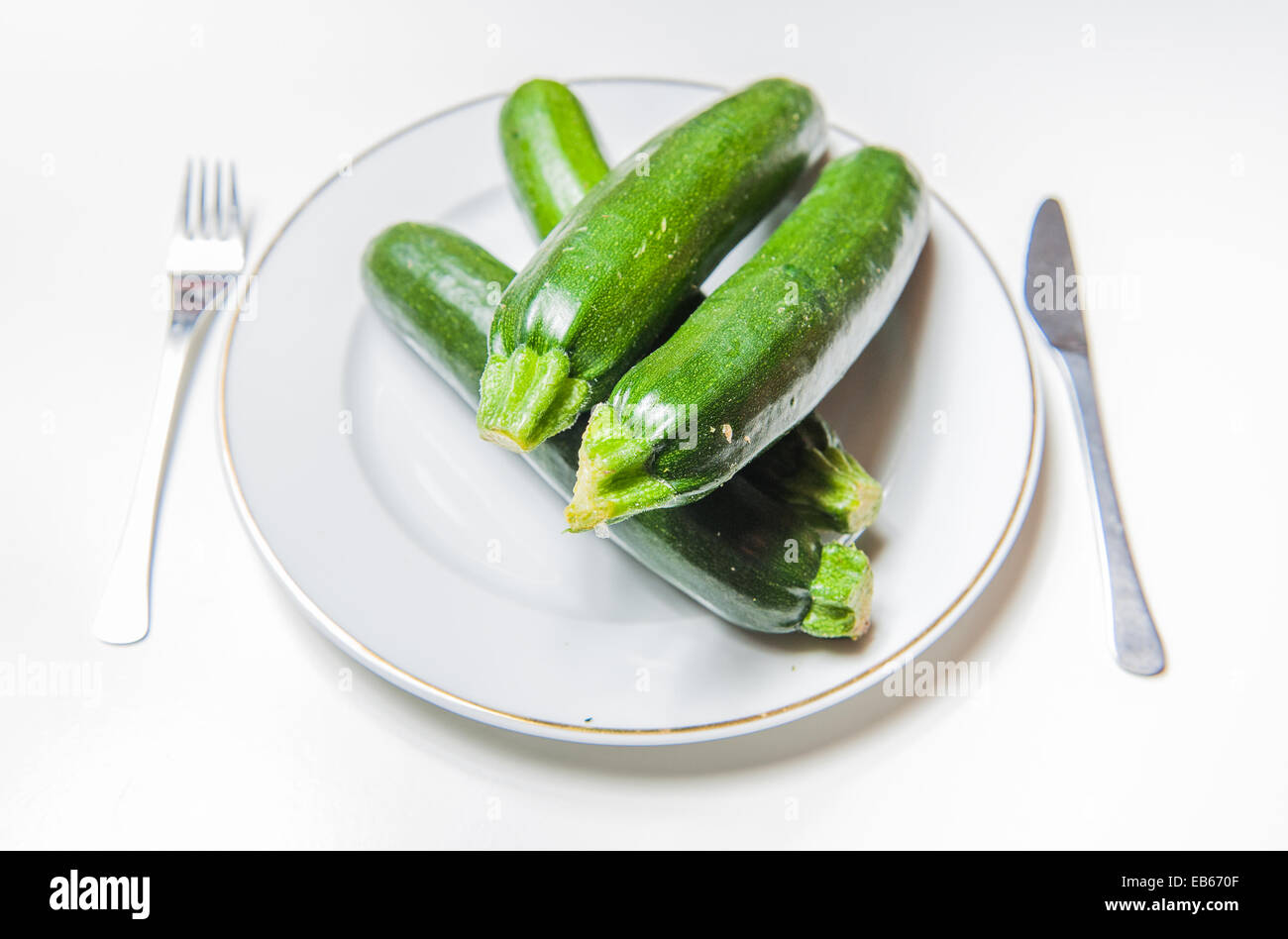 Rohe frische Zucchini auf einem weißen Teller mit weißem Hintergrund mit einer Gabel und einem Messer Stockfoto
