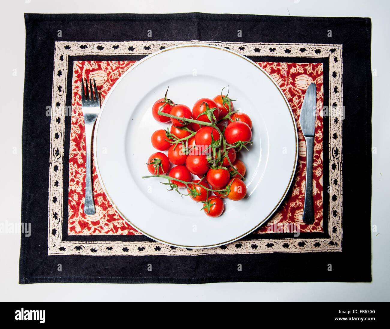 Rohe Tomaten Pachino-Klasse auf einem weißen Teller mit einer Gabel und einem Messer Stockfoto