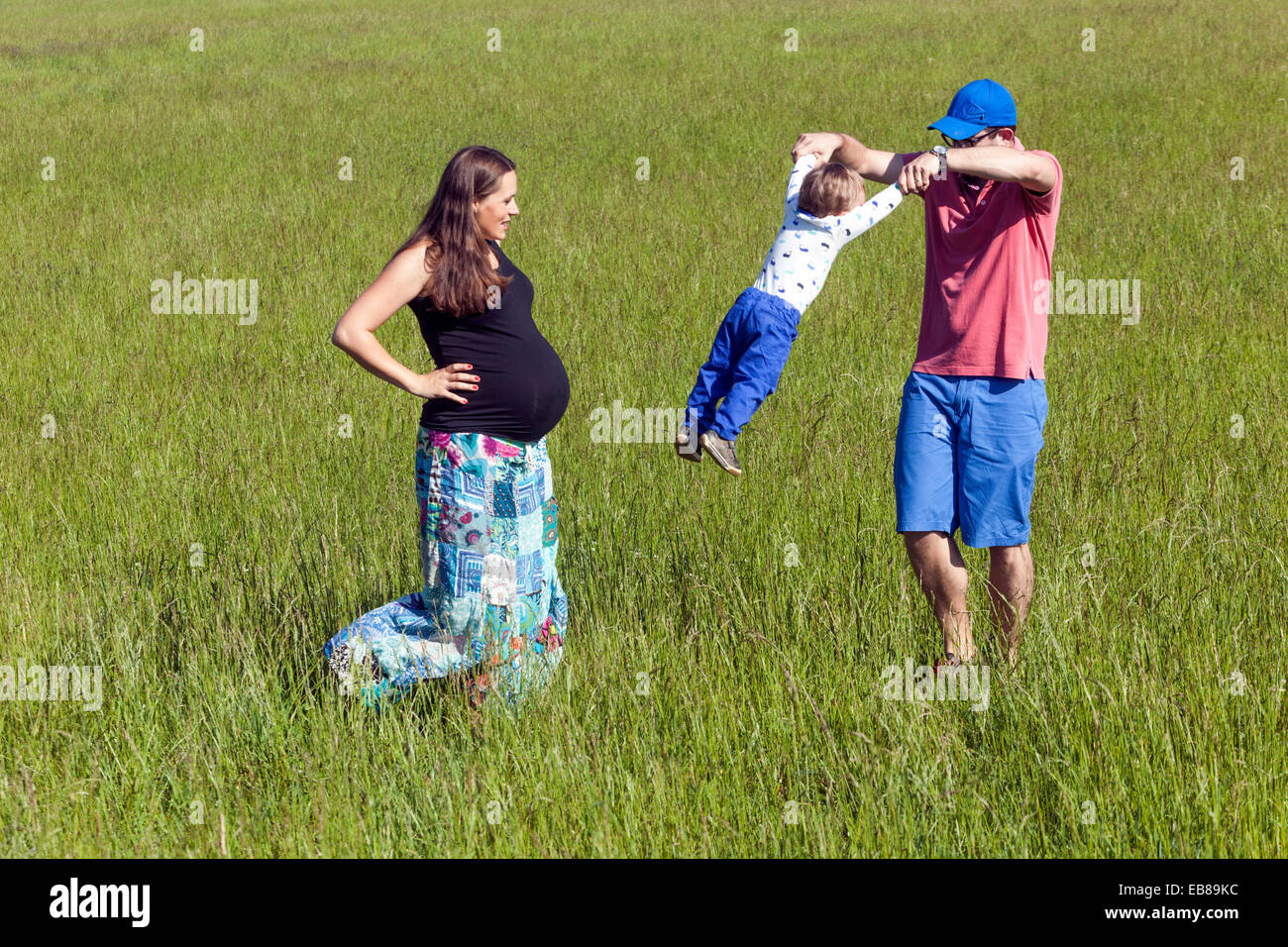 Eine glückliche Familie, eine schwangere Frau mit ihrem Mann und kleiner Junge Zeit miteinander verbringen und spielen in einer Sommerwiese Stockfoto